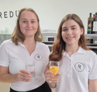 Diätologinnen Johanna Obermann und Carolina Richter mit einem Glas in der Hand als Zeichen, dass man auf ausreichend Flüssigkeitszufuhr achten soll.