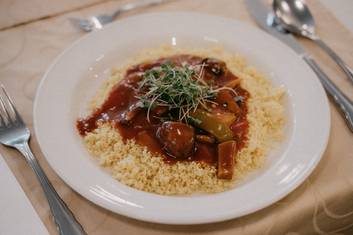 Teller mit Seitan Geschnetzeltem mit Pilzen und Cous Cous am Tisch im Kurrestauranat